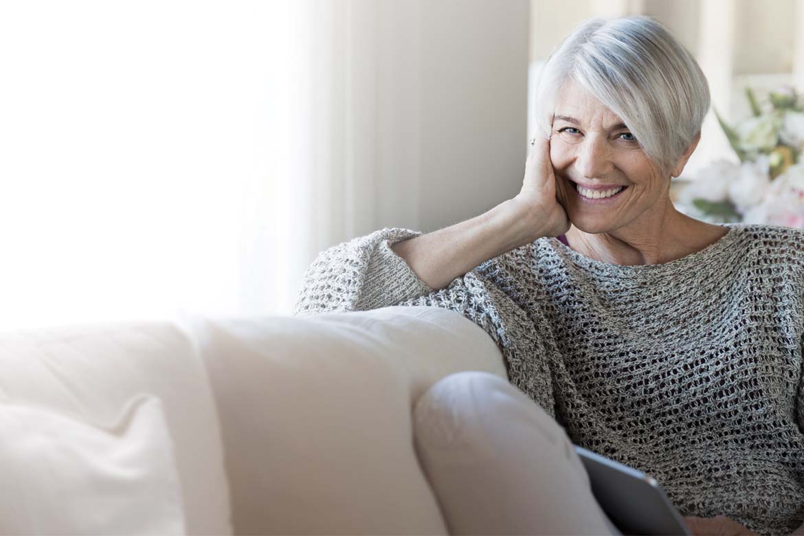 A retired woman relaxing on a couch with a tablet
