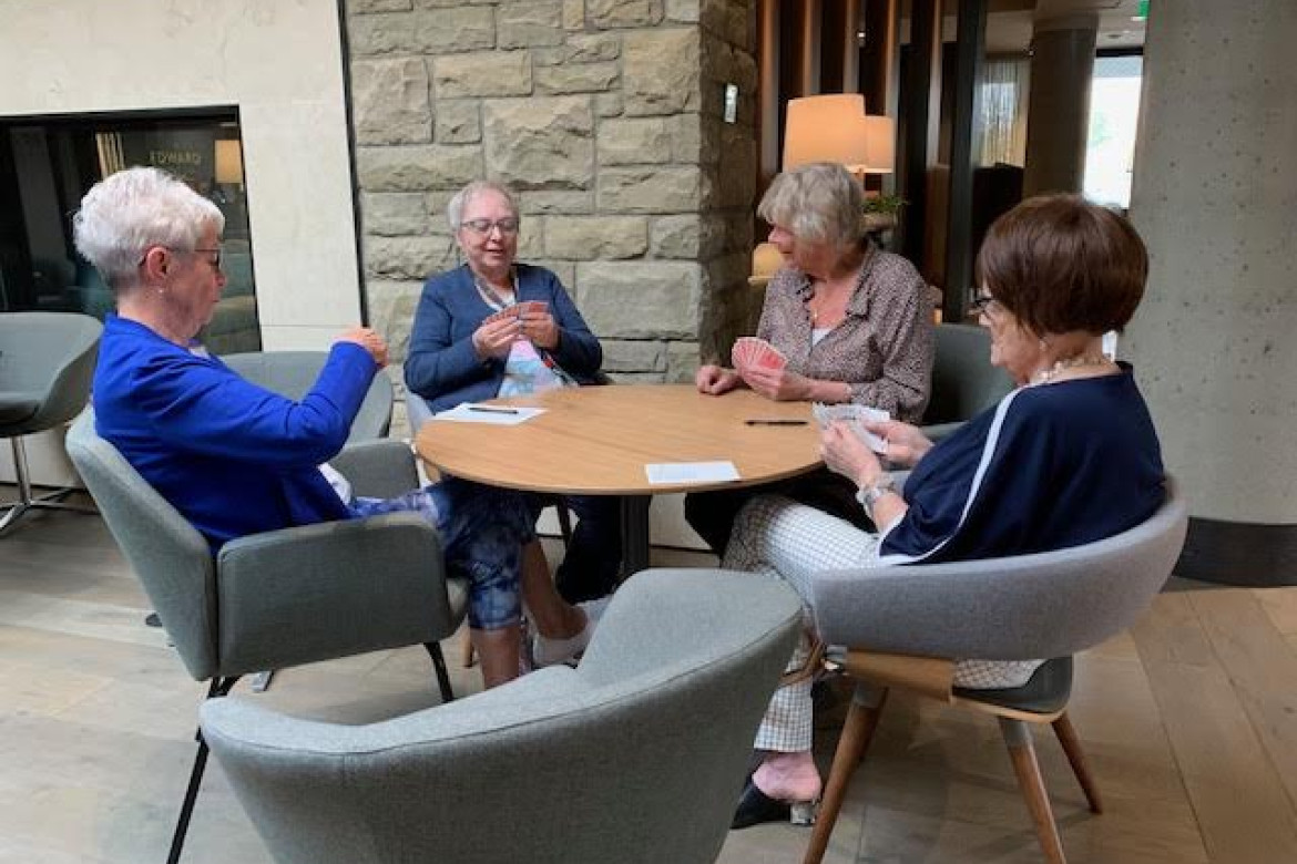 Four senior ladies seated around a table playing cards