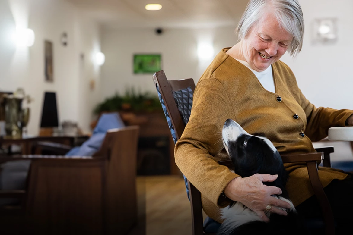Senior seated and smiling with her dog.