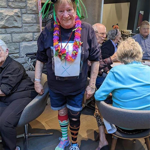 Senior resident dressed in a goofy halloween costume with different coloured socks, a lei, and a fun hat.