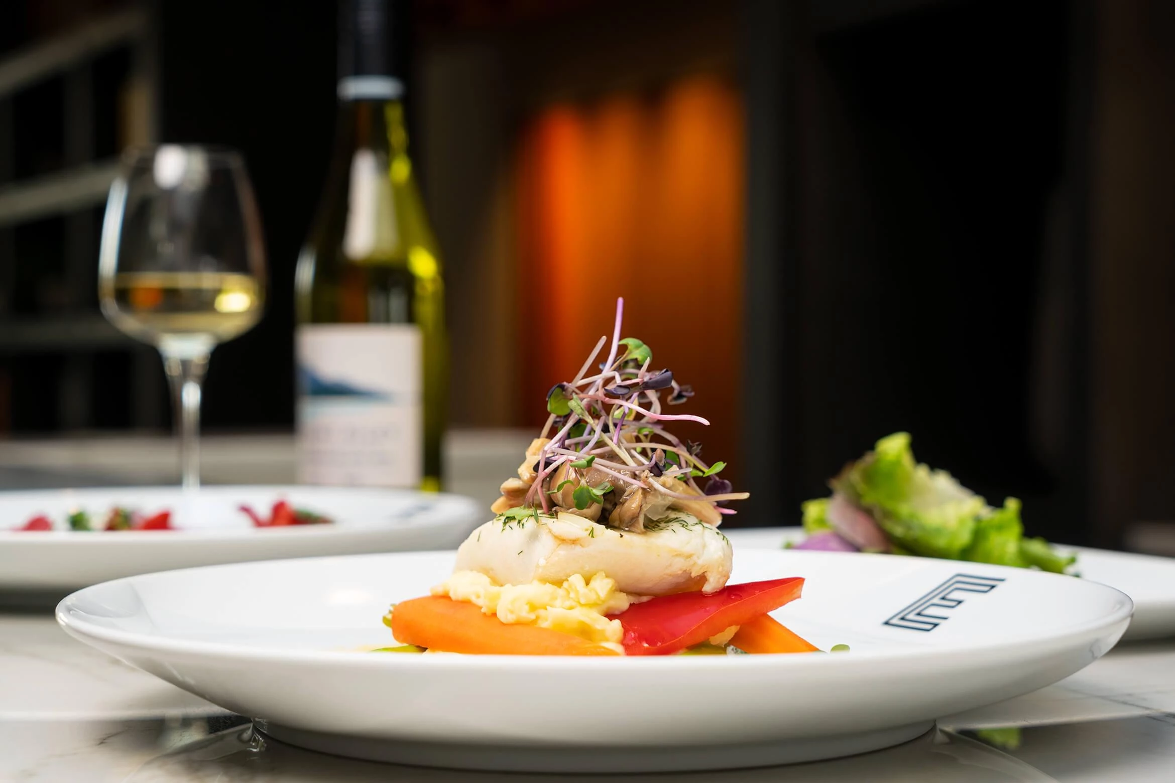 An Edward plate of white fish and vegetables beside a bottle of white wine.