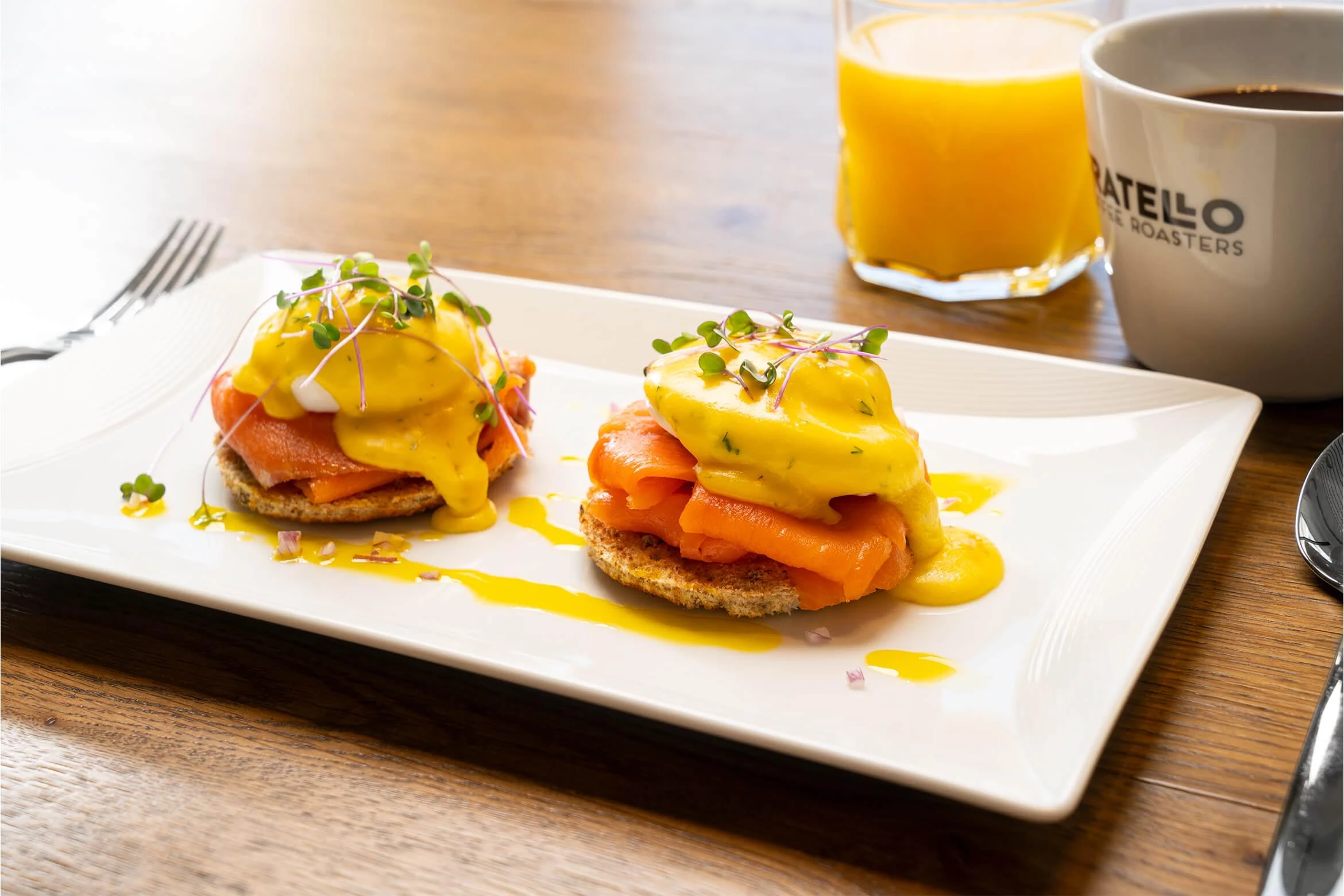 A plate featuring smoked salmon Benedict with coffee and orange juice.